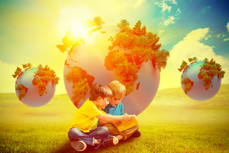 Pupils reading book against blue sky over green fieldの写真素材