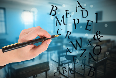 Businesswomans hand writing with fountain pen against empty classroomの写真素材