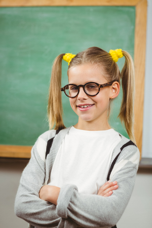 Portrait of cute pupil posing with arms crossed in a classroom in schoolの写真素材