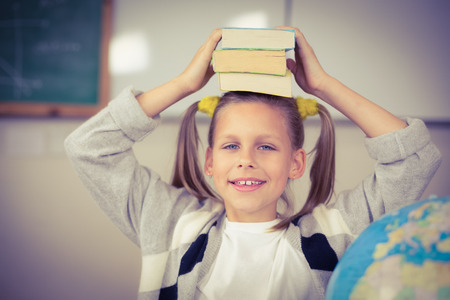Portrait of cute pupil balancing books on head in a classroom in schoolの写真素材