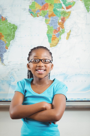 Portrait of cute pupil standing in front of world map in a classroomの写真素材