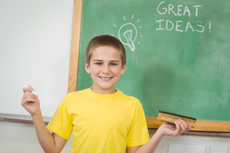 Portrait of smiling pupil holding chalk in front of chalkboard in school