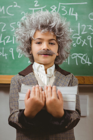 Portrait of little Einstein holding books in front of chalkboard in a classroomの写真素材