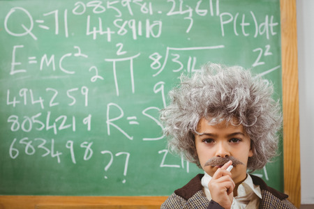 Portrait of little Einstein thinking in front of chalkboard in a classroomの写真素材
