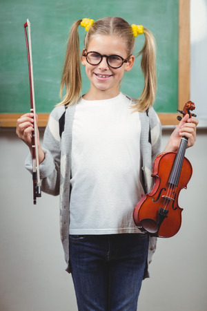 Portrait of cute pupil holding violin in a classroom in schoolの写真素材