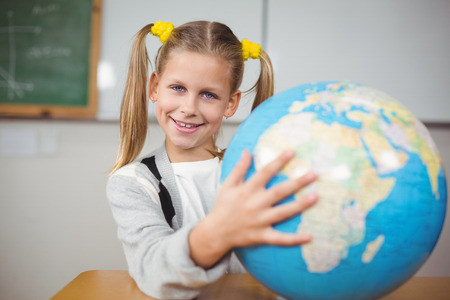Portrait of cute pupil holding globe in a classroom in schoolの写真素材