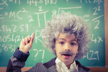 Portrait of little Einstein having an idea in front of chalkboard in a classroomの写真素材