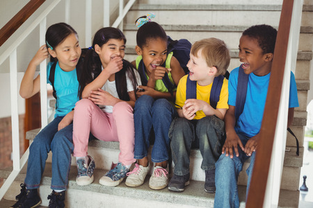 Happy pupils laughing and sitting on stairs in schoolの写真素材