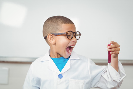 Surprised pupil with lab coat looking at test tube in a classroomの写真素材