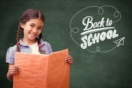 Cute pupil smiling at camera during class presentation against green chalkboard