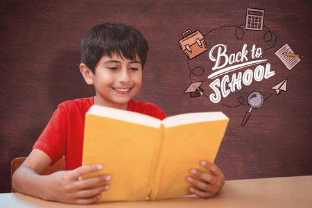 Cute boy reading book in library against desk