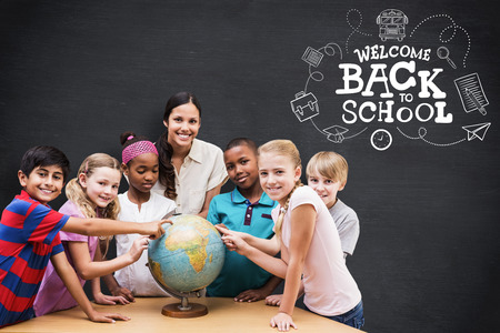 Cute pupils and teacher looking at globe in library against blackboardの写真素材
