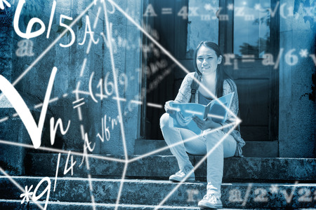 Math problems against smiling student sitting and holding bookの写真素材