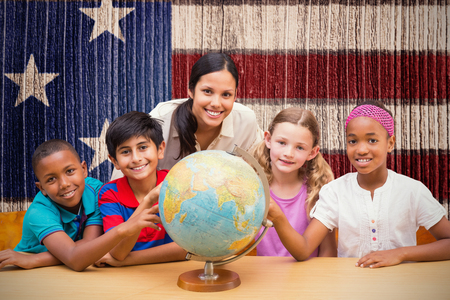 Cute pupils and teacher looking at globe in library  against composite image of usa national flagの写真素材