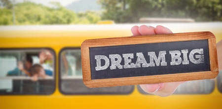 The word dream big and hand showing chalkboard against cute pupils smiling at camera in the school busの写真素材