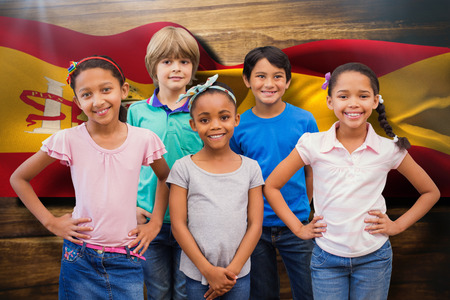 Cute pupils smiling at camera in classroom against digitally generated spain flag ripplingの写真素材