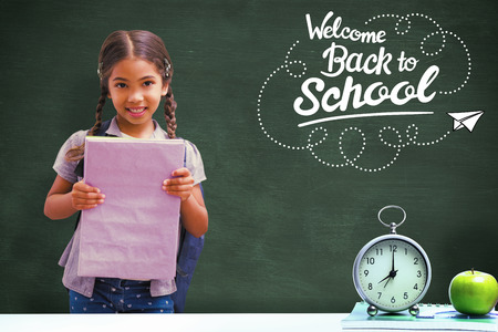 Cute pupil smiling at camera holding notepad  against green chalkboard
