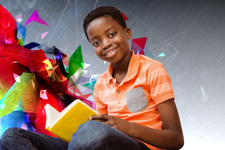Cute boy reading book in library against geometric design