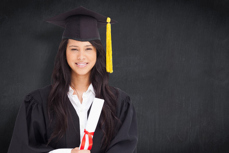 A smiling woman looking at the camera while dressed in her graduation gown  against blackboardの写真素材