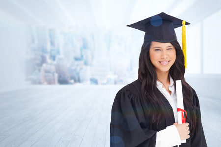 A smiling woman holding her degree as she has graduated from university against city scene in a roomの写真素材