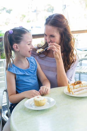 Mother and daughter enjoying cakes at cafe terrace on a sunny dayの写真素材