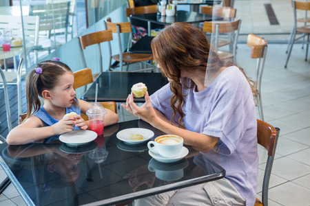 Mother and daughter enjoying cakes in coffee shopの写真素材