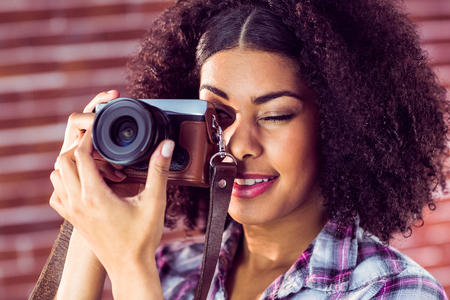 Attractive young woman photographing with camera against red brick background