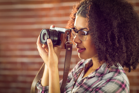 Attractive hipster photographing with camera against red brick backgroundの写真素材