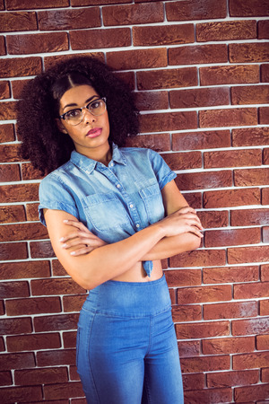 Portrait of attractive hipster with arms crossed leaning against red brick backgroundの写真素材