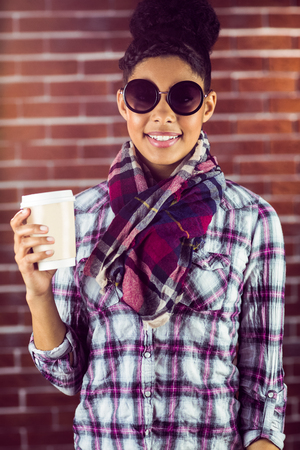 A female hipster holding a cup of coffee against a brick wallの写真素材