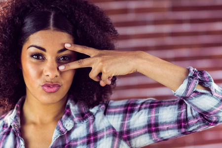 Portrait of attractive young woman showing peace sign against red brick backgroundの写真素材