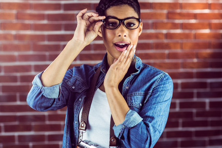 Portrait of a gorgeous hipster posing with glasses against red brick backgroundの写真素材