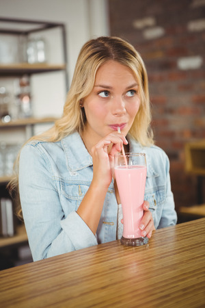 Pretty blonde drinking smoothie through straw at coffee shopの写真素材