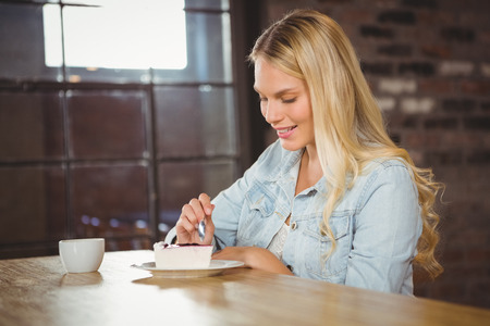 Smiling blonde eating cake and having coffee at coffee shopの写真素材