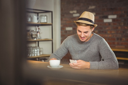 Handsome hipster having coffee and using smartphone at coffee shopの写真素材