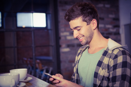Smiling hipster sitting and texting at coffee shopの写真素材