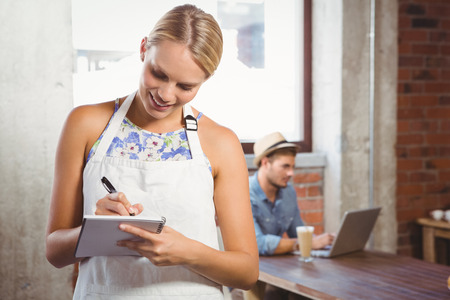 Smiling blonde waitress taking order in front of customer at coffee shopの写真素材