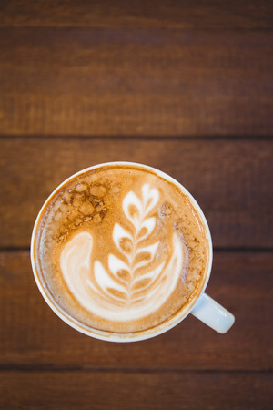 Cup of cappuccino with coffee art on wooden table at coffee shopの写真素材