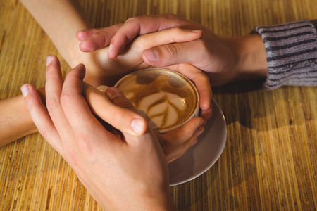 Couple holding hands around cappuccino with coffee art at coffee shopの写真素材