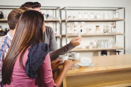 Group of friends looking at a smartphone in a cafeの写真素材