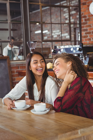 Two smiling friends having coffee at coffee shopの写真素材