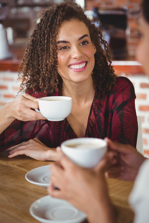 Two smiling friends having coffee at coffee shopの写真素材
