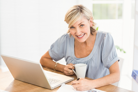 Portrait of a smiling businesswoman working on a laptop at officeの写真素材