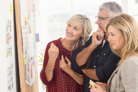 Smiling business team looking at notes on the wall at officeの写真素材