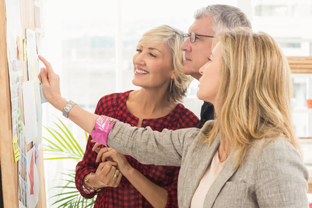 Smiling business team pointing a note on the wall at officeの写真素材