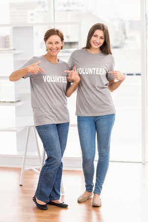 Portrait of smiling female volunteers showing their shirts in the officeの写真素材