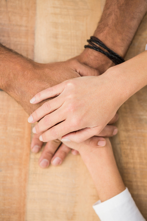 Casual business colleagues stacking their hands on wooden deskの写真素材