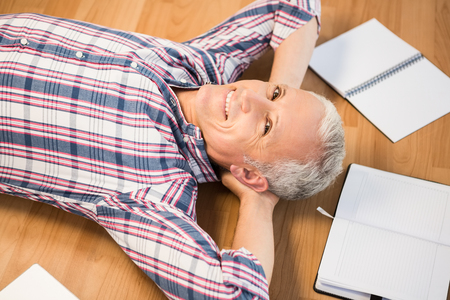 Portrait of smiling man lying on floor surrounded by office itemsの写真素材