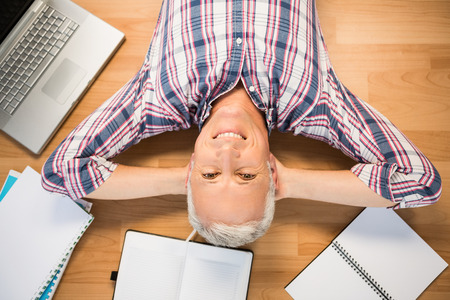 Portrait of smiling man lying on floor surrounded by office itemsの写真素材
