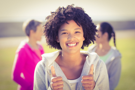 Portrait of sporty woman doing thumbs up in front of friends in parklandの写真素材